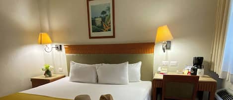 Habitación de hotel con una cama, dos mesitas de noche, un escritorio, una silla y un cuadro en la pared.