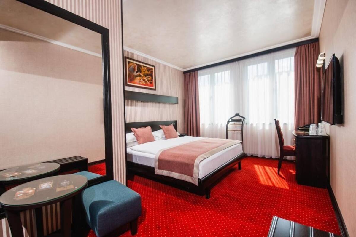 A hotel room with a bed, a desk, a chair, a TV, and a window with curtains.