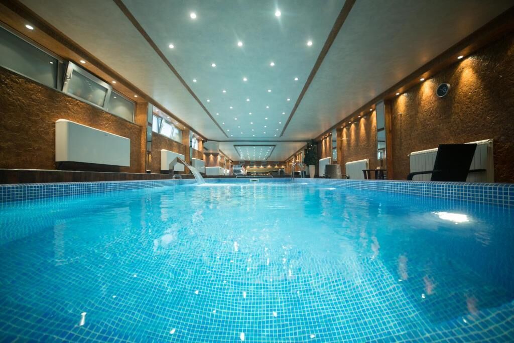 Una piscina interior con agua azul cristalina, paredes de madera e iluminación en el techo.