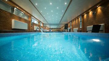 Una piscina interior con agua azul cristalina, paredes de madera e iluminación en el techo.