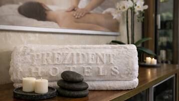 A towel with 'PREZIDENT HOTELS' embossed, a stack of stones, and two lit candles on a wooden surface.