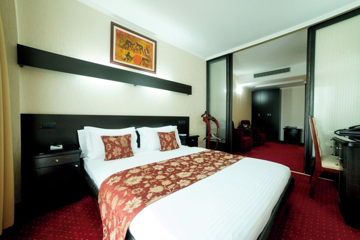 A hotel room with a large bed, a nightstand, a desk, and a chair.