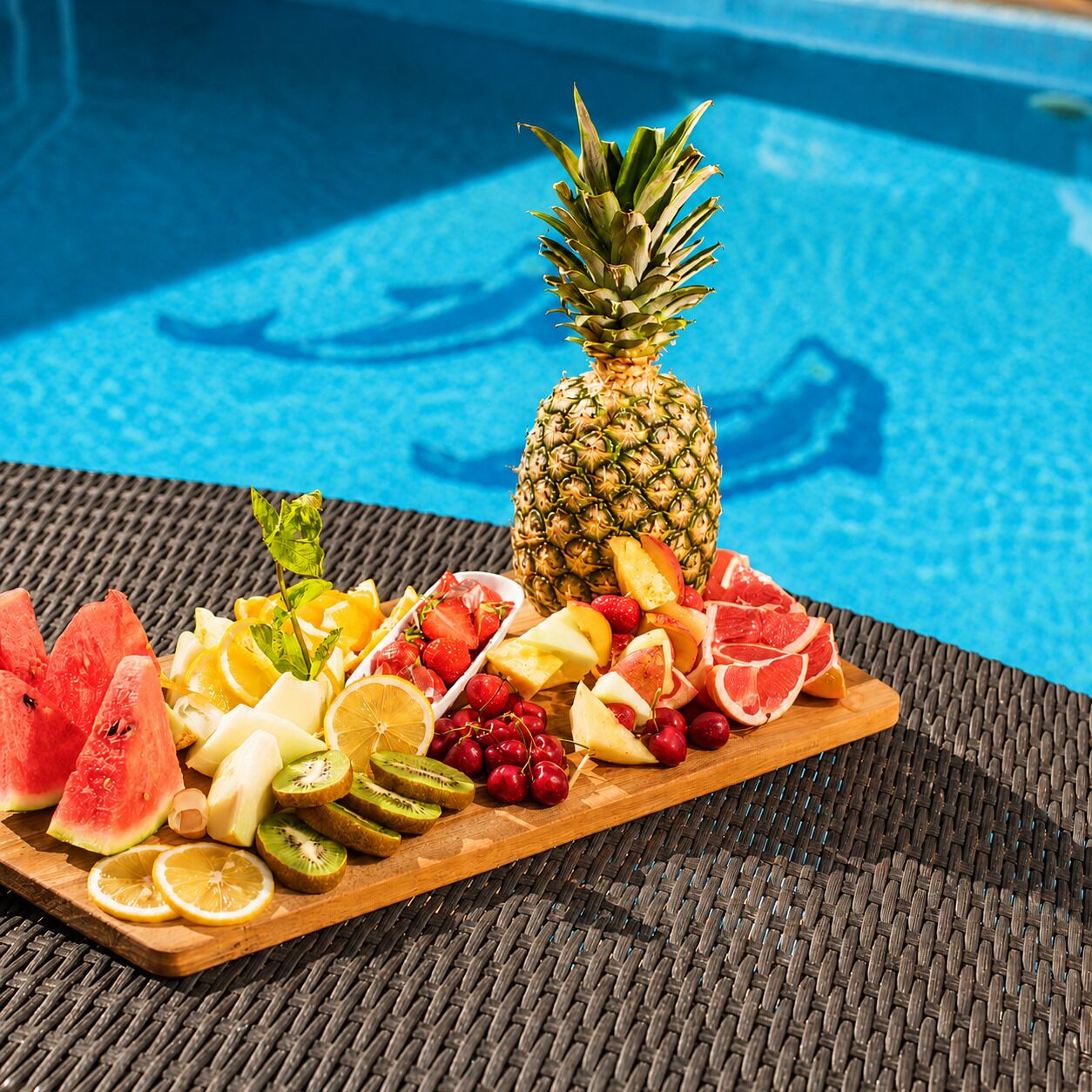 Una bandeja de fruta con una piña junto a una piscina.