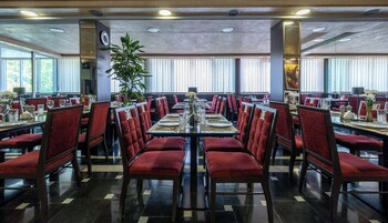 Un comedor amplio con sillas tapizadas rojas, una mesa central dispuesta para comer y grandes ventanales que dejan entrar luz natural.