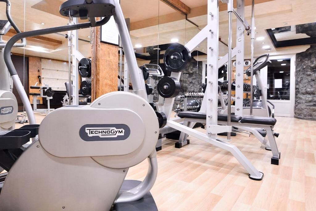 Une salle de sport équipée de divers appareils d’exercice, notamment un appareil Technogym, des supports à poids et des appareils de cardio.
