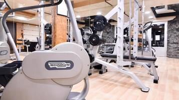 Une salle de sport équipée de divers appareils d’exercice, notamment un appareil Technogym, des supports à poids et des appareils de cardio.