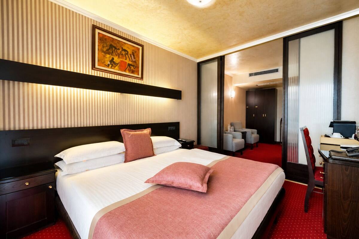 A hotel room with a large bed, a desk, a chair, and a wardrobe.