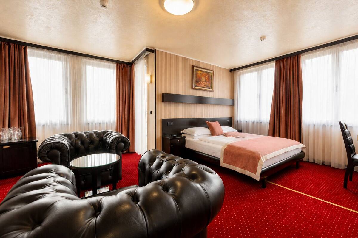 A hotel room with a bed, a leather armchair, a small round table, and a TV.