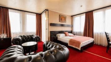Una habitación de hotel con cama, un sillón de cuero, una mesita redonda y televisión.
