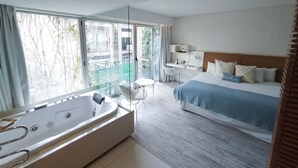 A modern hotel room with a large window, a separate desk area, a separate chair, a large bed, and a separate bathroom with a bathtub. - CasaCalma Hotel (Buenos Aires)
