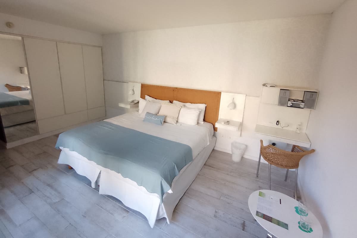 A modern hotel room with a large bed, bedside tables, a small table, and a chair.