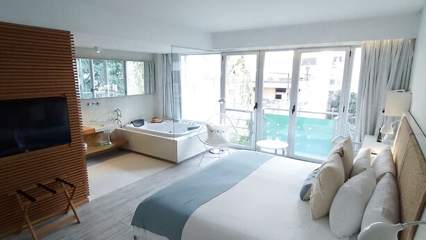 A modern hotel room with a large bed, a bathtub, a TV, and a balcony with a view. - CasaCalma Hotel (Buenos Aires)
