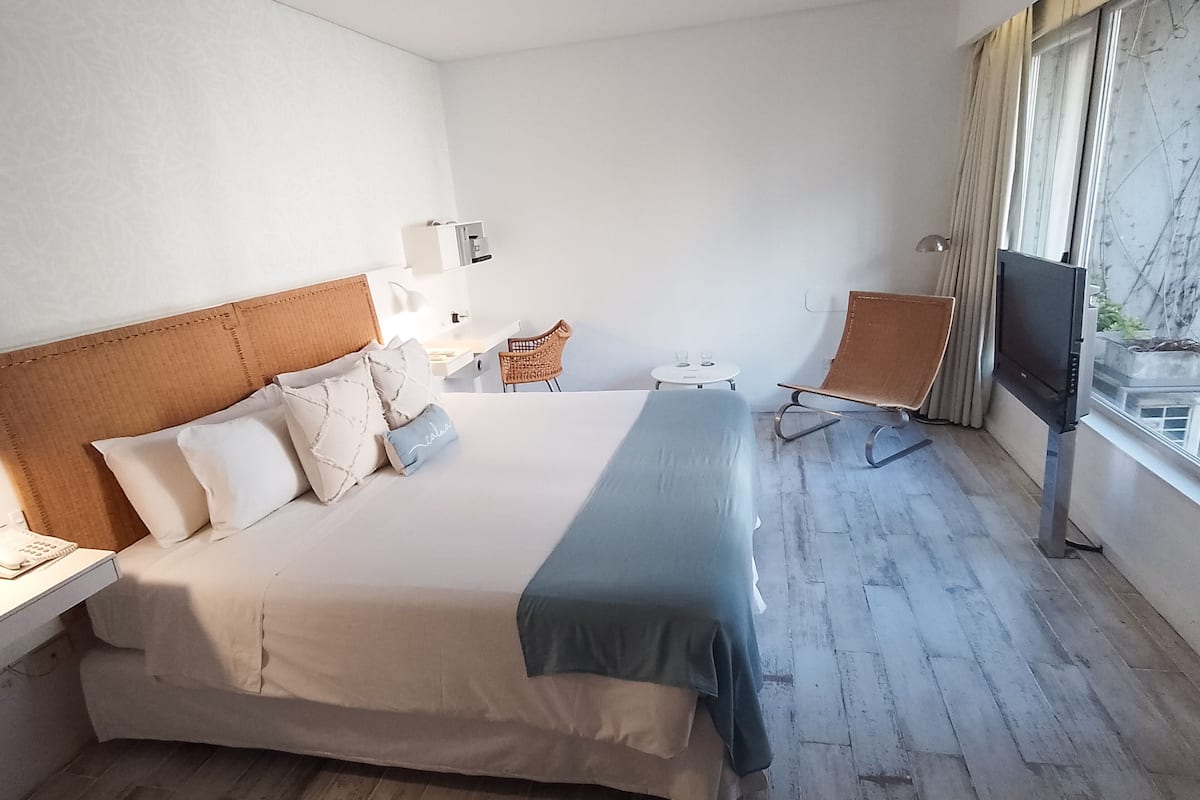 A hotel room with a large bed, a TV, a chair, and a small table.