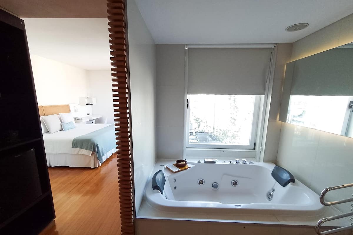 A modern bathroom with a bathtub, a window with a view, and a wooden floor.