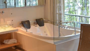 Un baño moderno con una bañera grande, cabina de ducha con mampara de vidrio y suelo de madera.