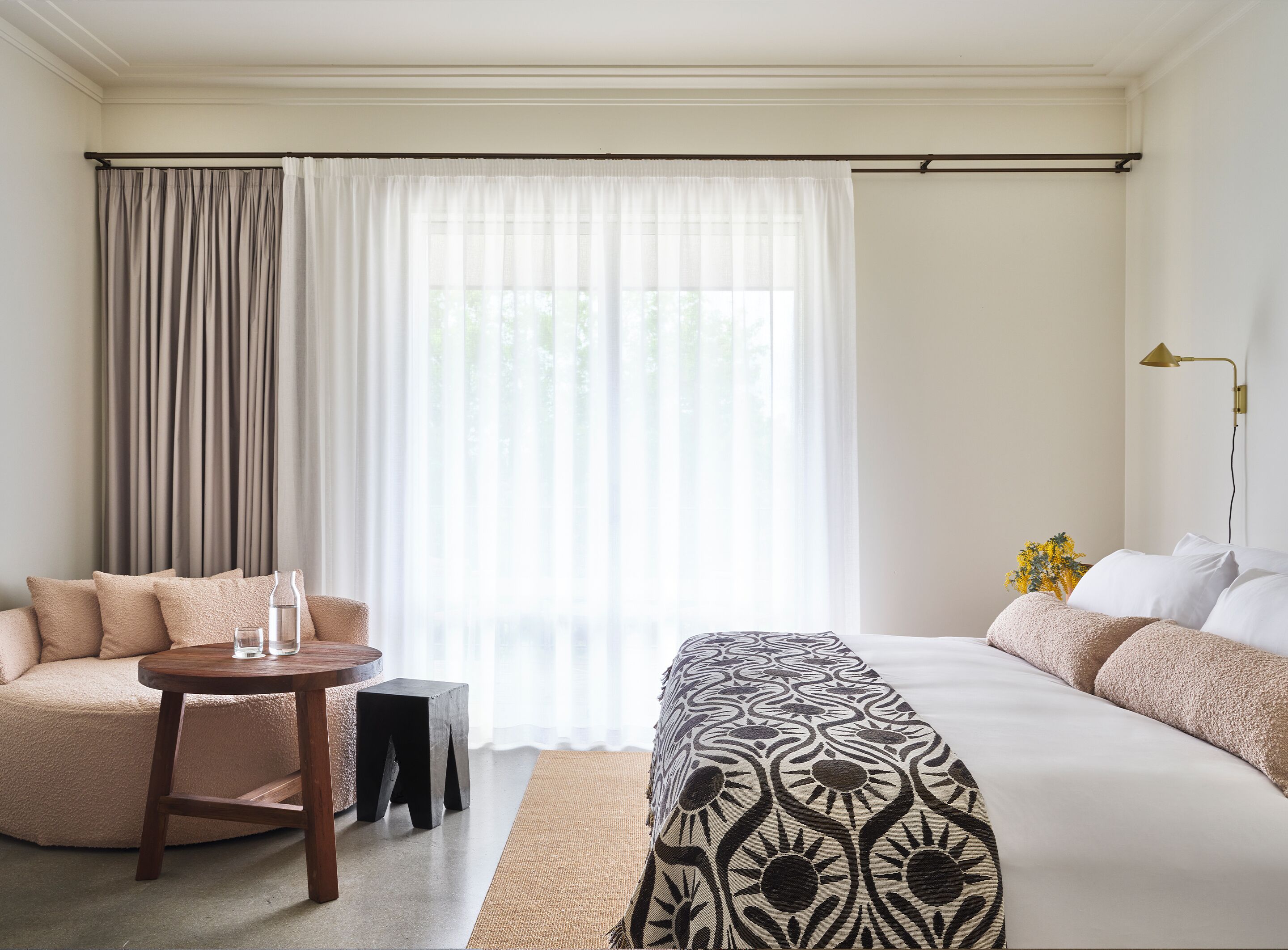 A hotel room with a bed, a sofa, a small table, and a lamp.