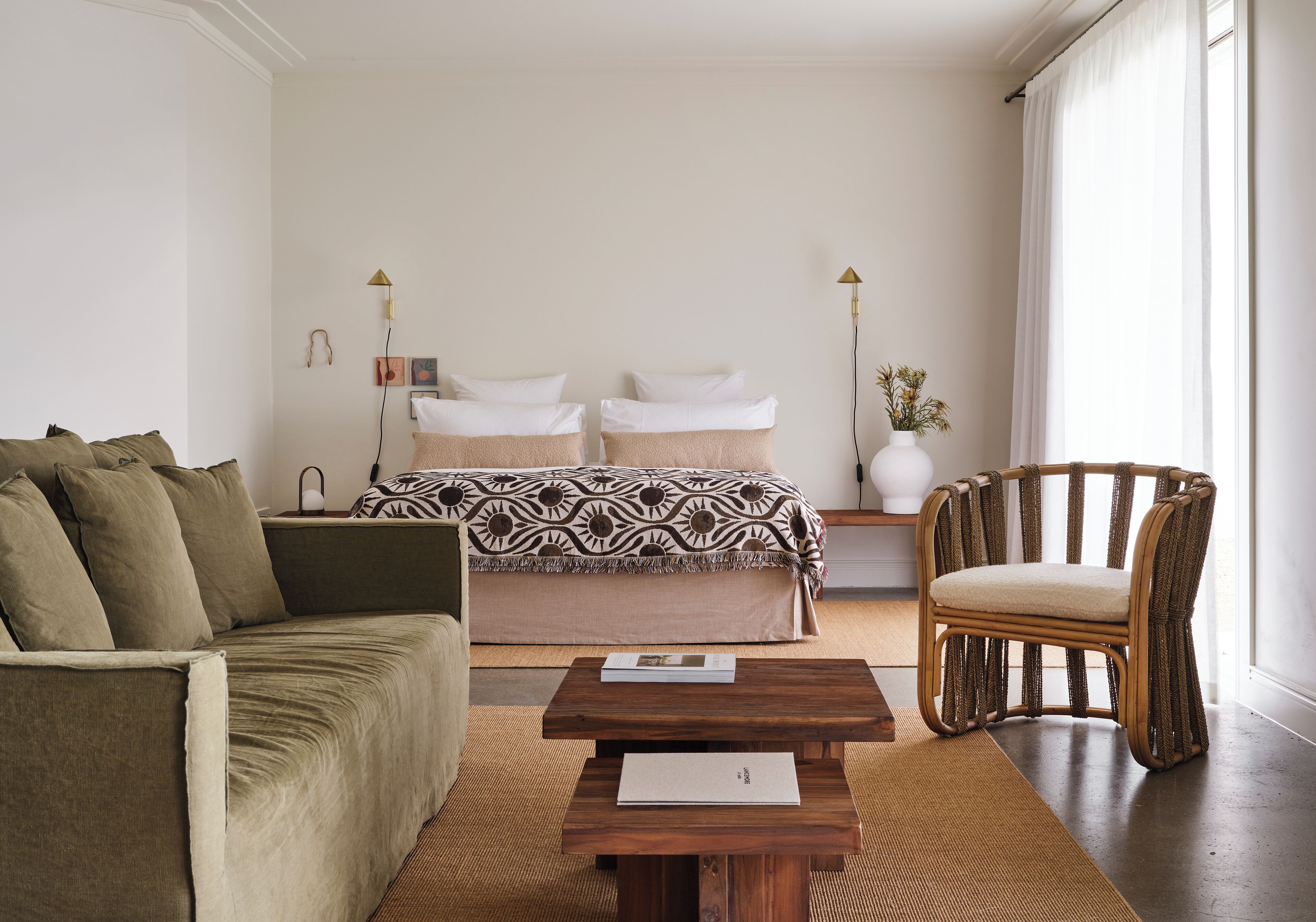 Un dormitorio con una cama, un sofá, una silla, una mesa de centro de madera y lámparas de noche.