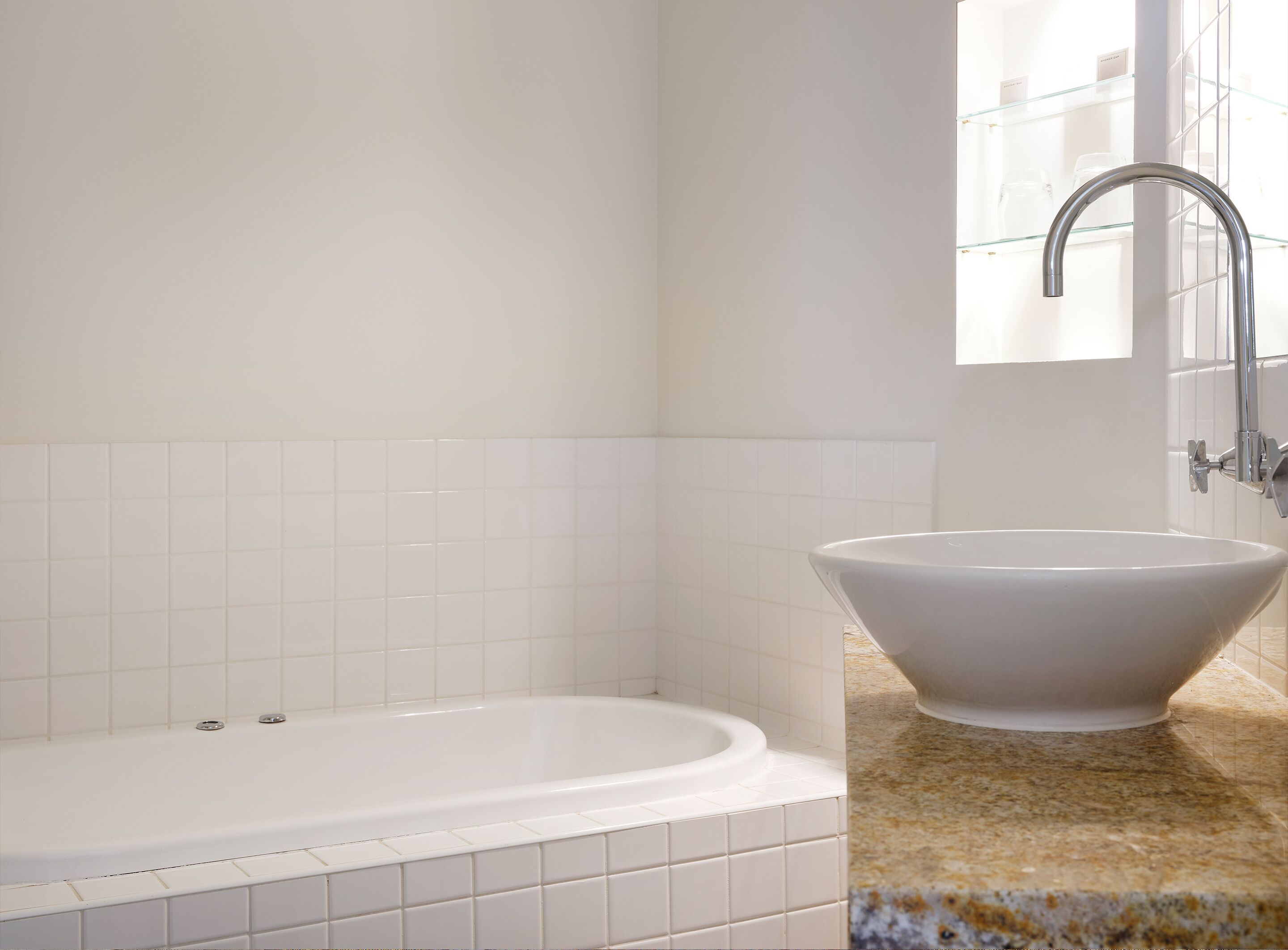 Un baño con una bañera blanca, un lavamanos blanco y un estante de vidrio con art ículos de aseo.