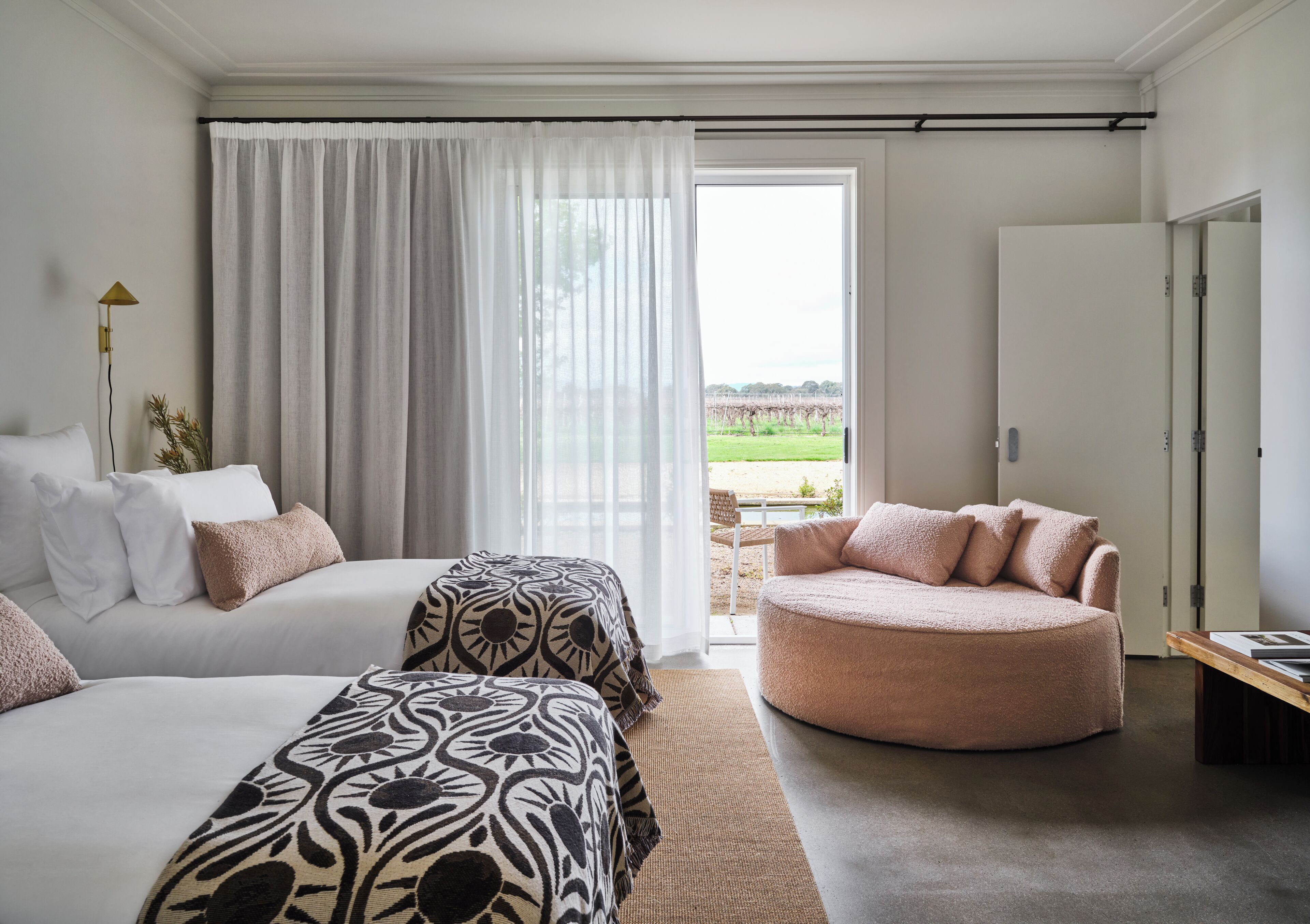 A hotel room with two beds, a round seating area, and a view of a green landscape through a large window.