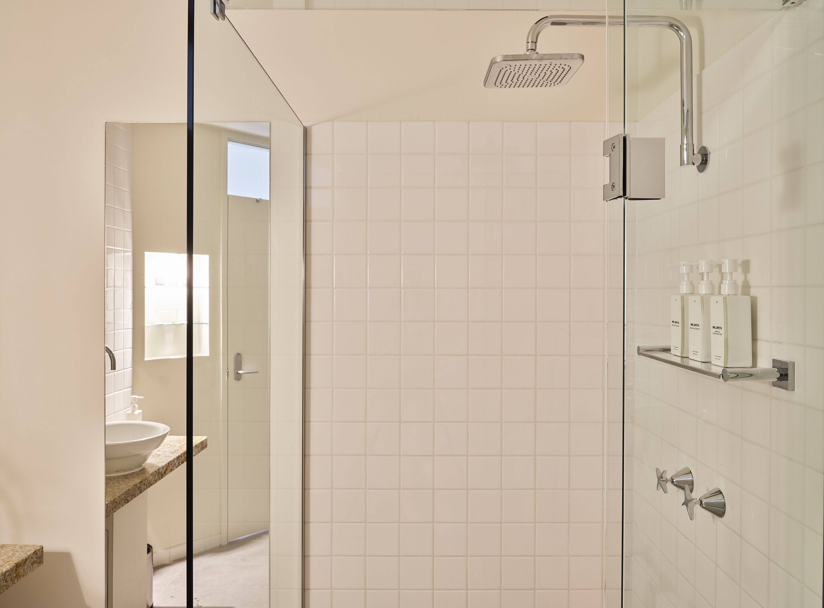 A modern bathroom with a glass shower enclosure, a sink with a countertop, and a shelf with toiletries.