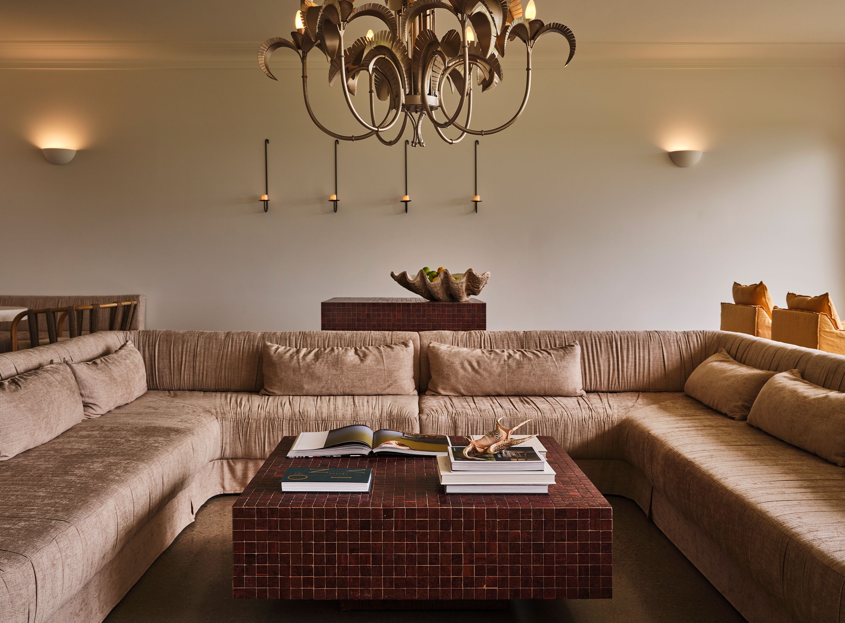 A modern living room with a sectional sofa, a coffee table with books, a decorative bowl, and a chandelier.