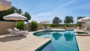 Piscina con sillas de descanso y sombrillas, rodeada de un patio con baldosas.