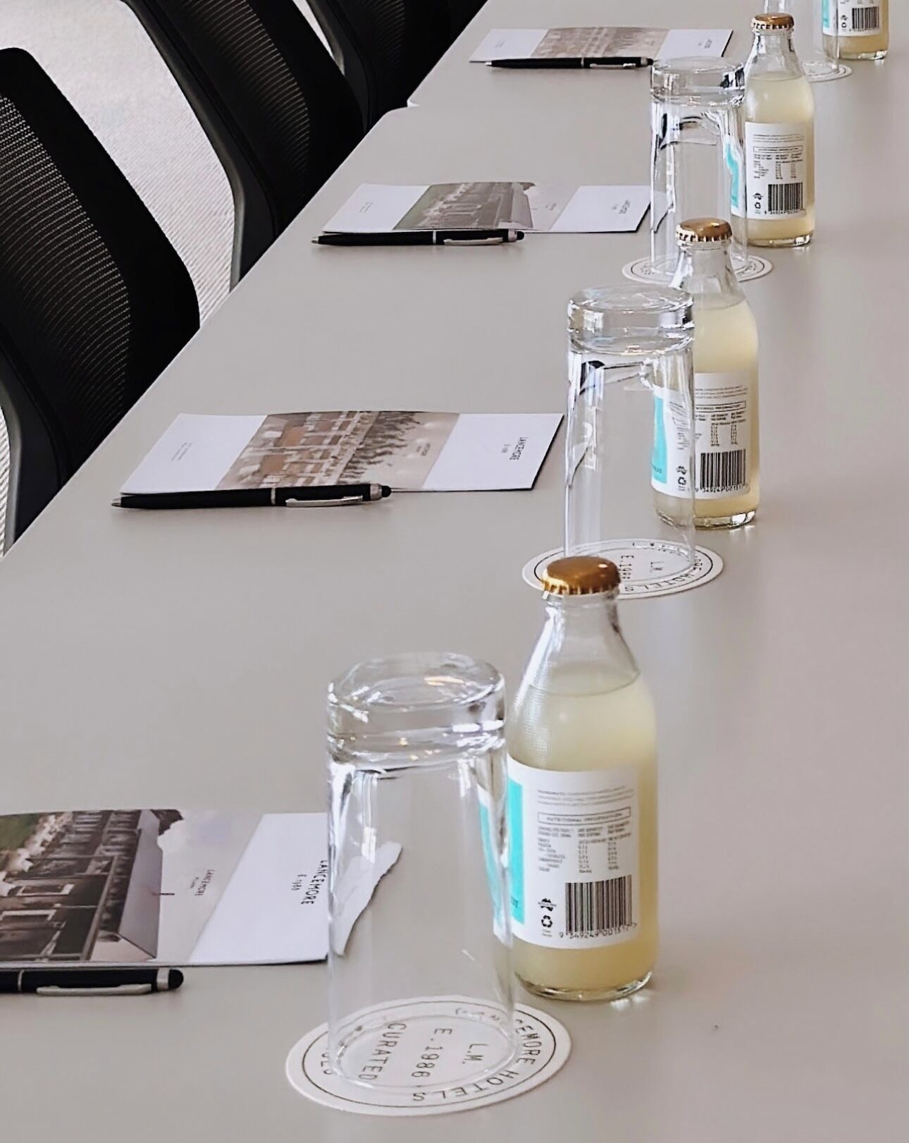 Una mesa de conferencias con documentos, bolígrafos y botellas de vidrio con bebida.