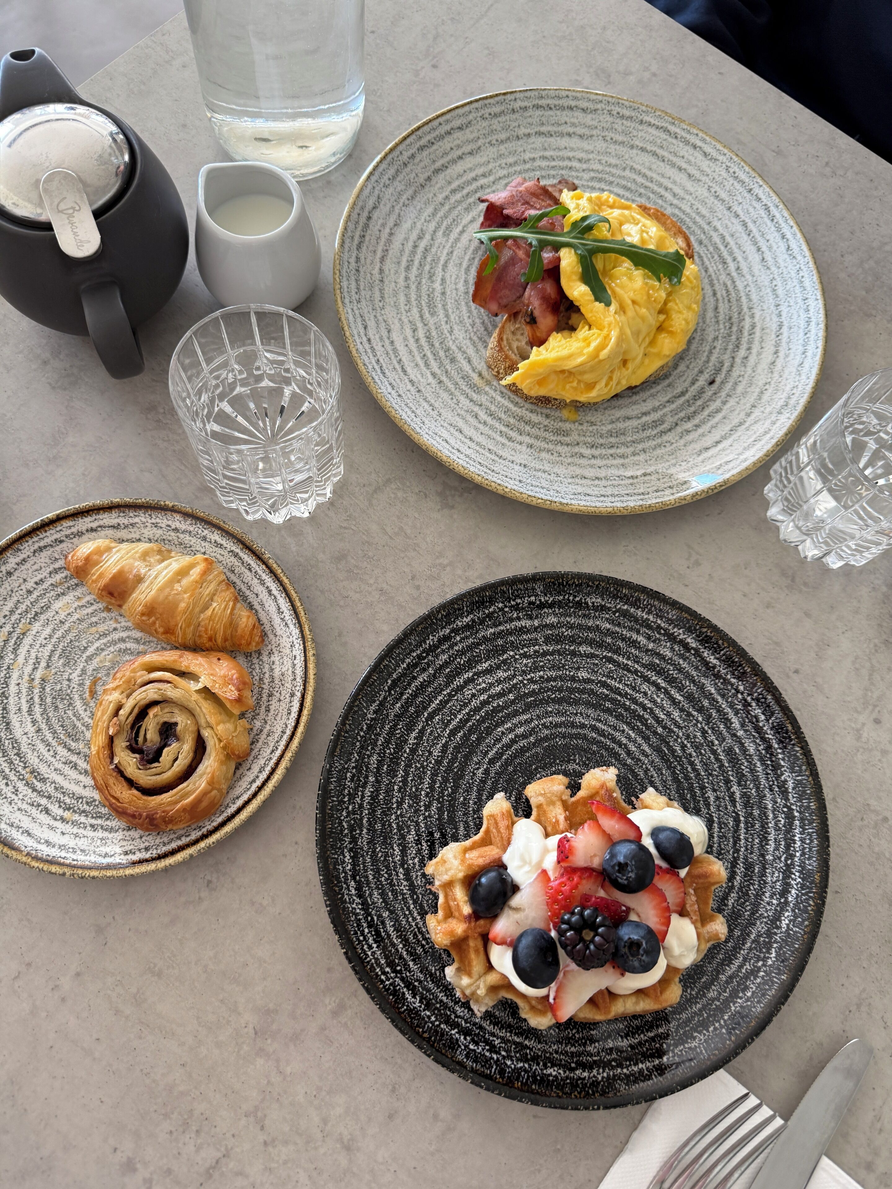 Een ontbijttafel met croissants, wafels met bessen en roerei.