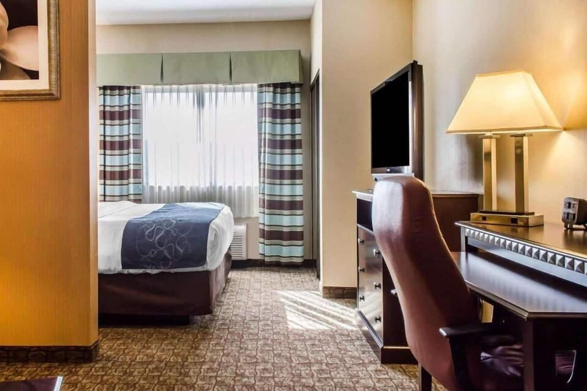 A hotel room with a bed, a desk with a lamp, a television, and a dresser.