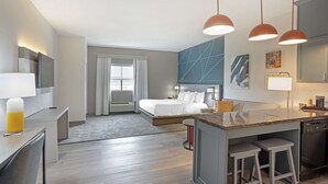 Een moderne hotelkamer met een bed, bureau en kitchenette.