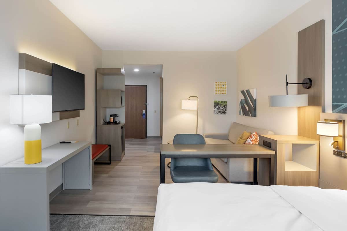 A modern hotel room with a bed, desk, chair, and a TV mounted on the wall.