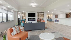 Een moderne hotel lobby met een grijze bank, een oranje fauteuil en een ronde tafel.