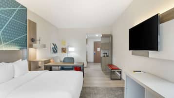 A hotel room with a large bed, a desk, a chair, a TV, and a small kitchenette.