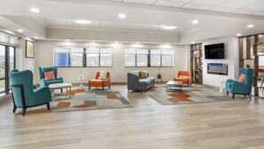Een ruime zithoek met blauwgroene fauteuils, een grijze bank en oranje stoelen.