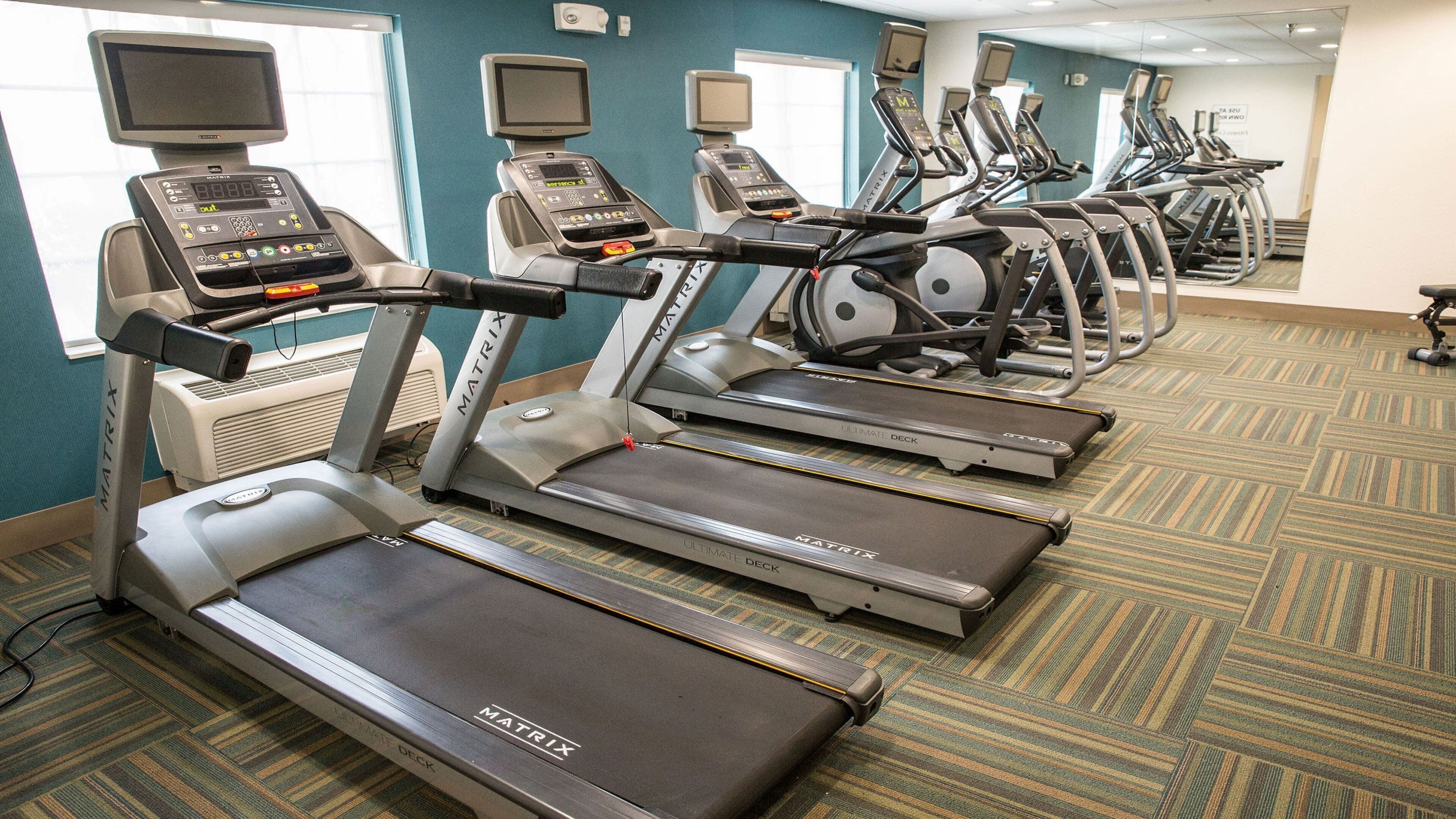 Un gimnasio con múltiples cintas de correr y bicicletas estáticas, suelo alfombrado y monitores de ejercicio.