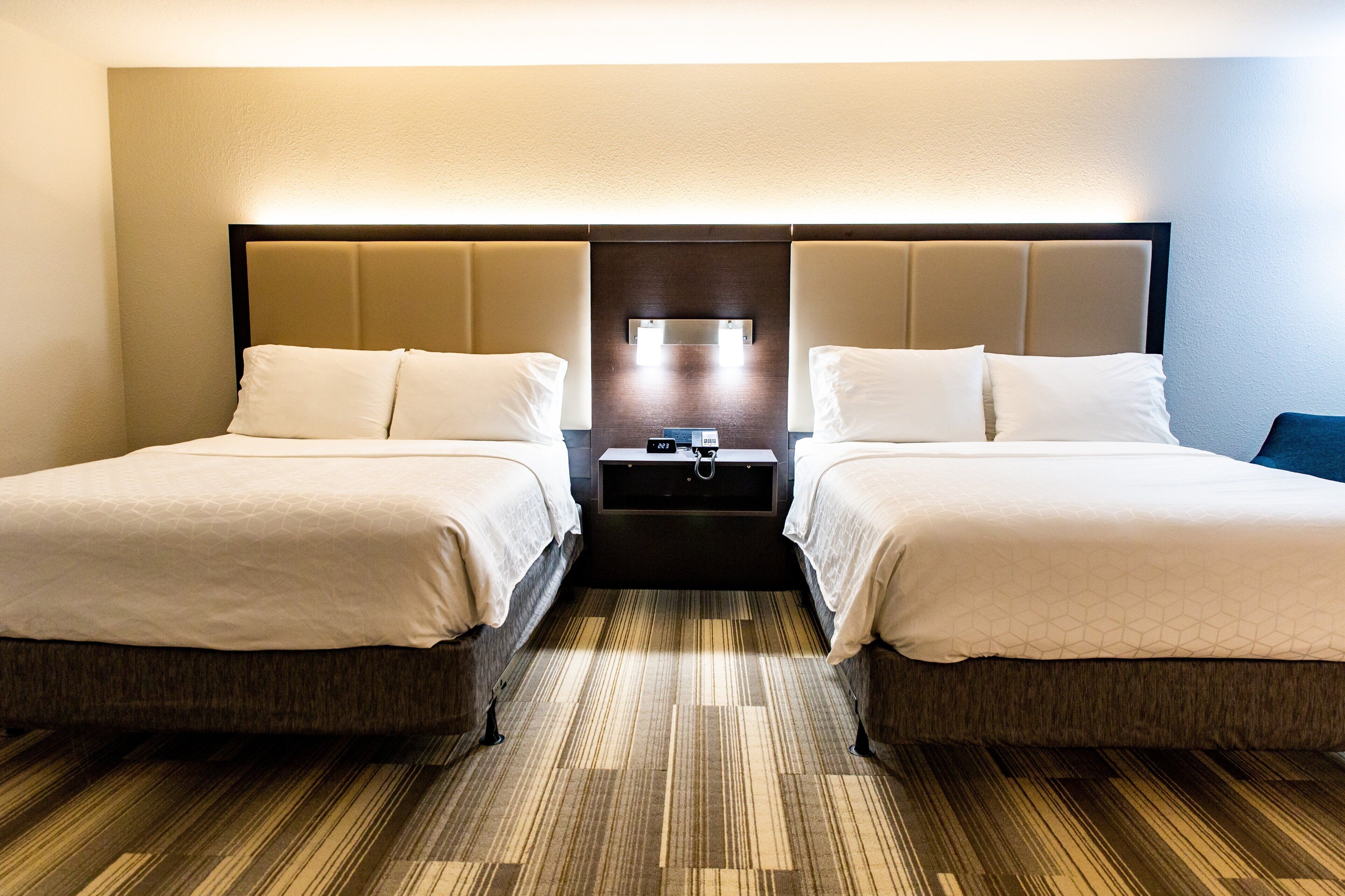 A hotel room with two beds, a nightstand, and a wall-mounted light.