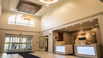 A hotel lobby with a reception desk, a glass door entrance, and a high ceiling with recessed lighting.