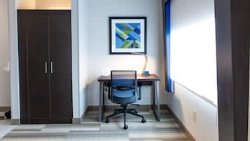 Una habitación con un armario de madera oscura, un escritorio con una silla y una obra de arte abstracta enmarcada en la pared.