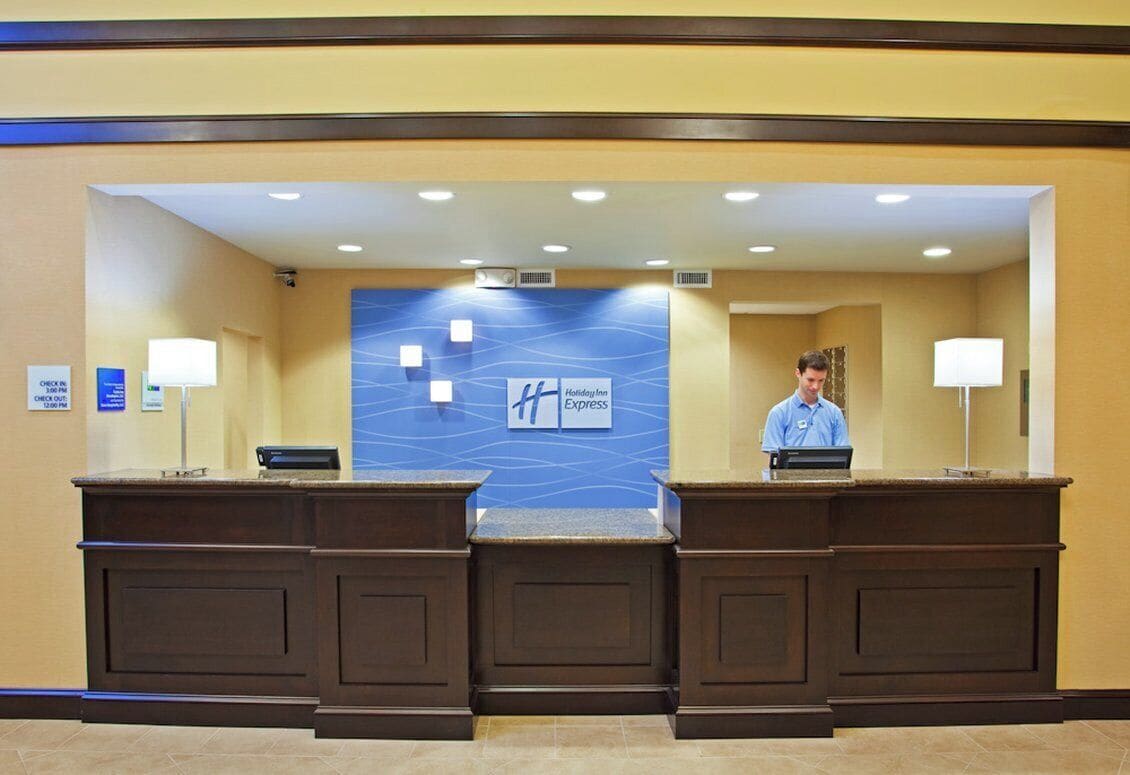 Una recepción de hotel con una pared azul que muestra el logotipo de Holiday Inn Express, dos recepcionistas y un mostrador de registro.