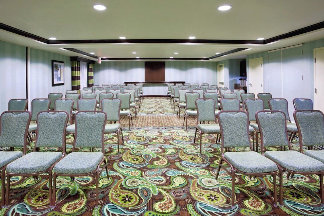 A conference room with rows of chairs, a carpeted floor, and a stage at the front.