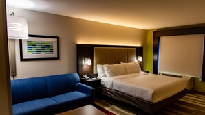 A hotel room with a bed, a blue sofa, a wooden table, a framed picture on the wall, and a window with blinds. - Holiday Inn Express Columbus-Dublin by IHG (Dublin)