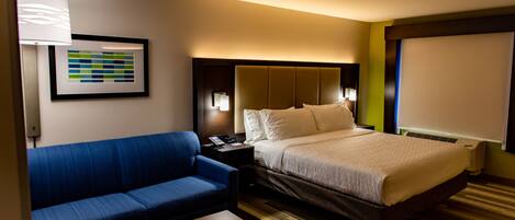 A hotel room with a bed, a blue sofa, a wooden table, a framed picture on the wall, and a window with blinds.