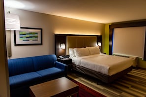 Habitació d'hotel amb un llit, un sofà blau, una taula de fusta, un quadre encadre on la paret i una finestra amb persianes.
