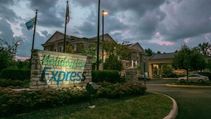 A Holiday Inn Express sign with American flags, surrounded by greenery and a building in the background. - Holiday Inn Express Columbus-Dublin by IHG (Dublin)