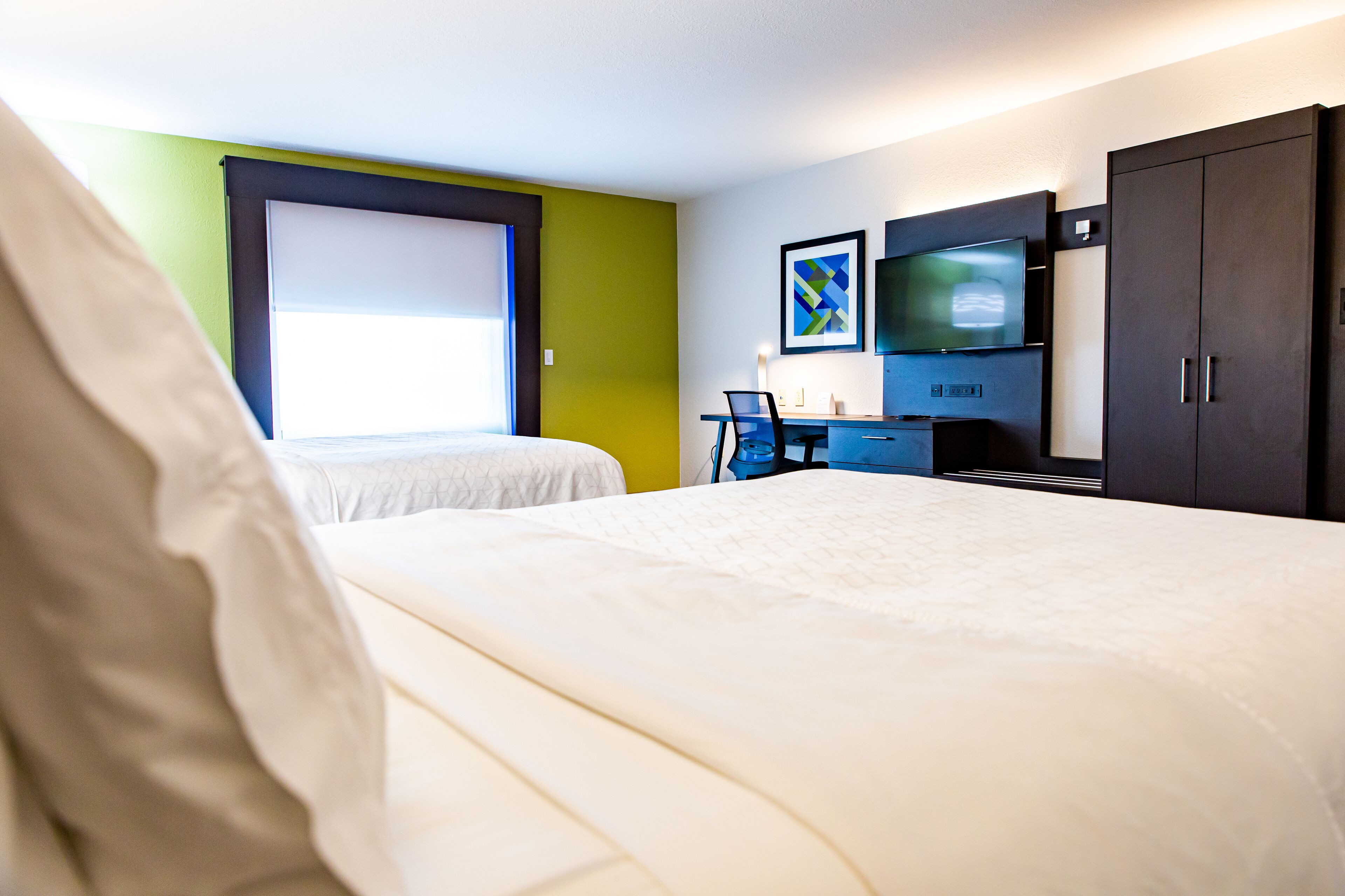A hotel room with two beds, a desk with a chair, a TV, and a wardrobe.