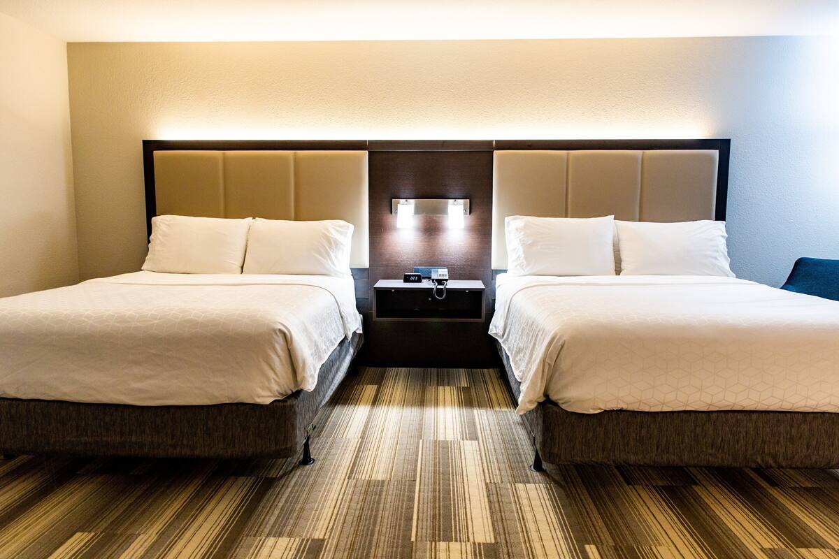 A hotel room with two beds, a nightstand, and a wall-mounted lamp.