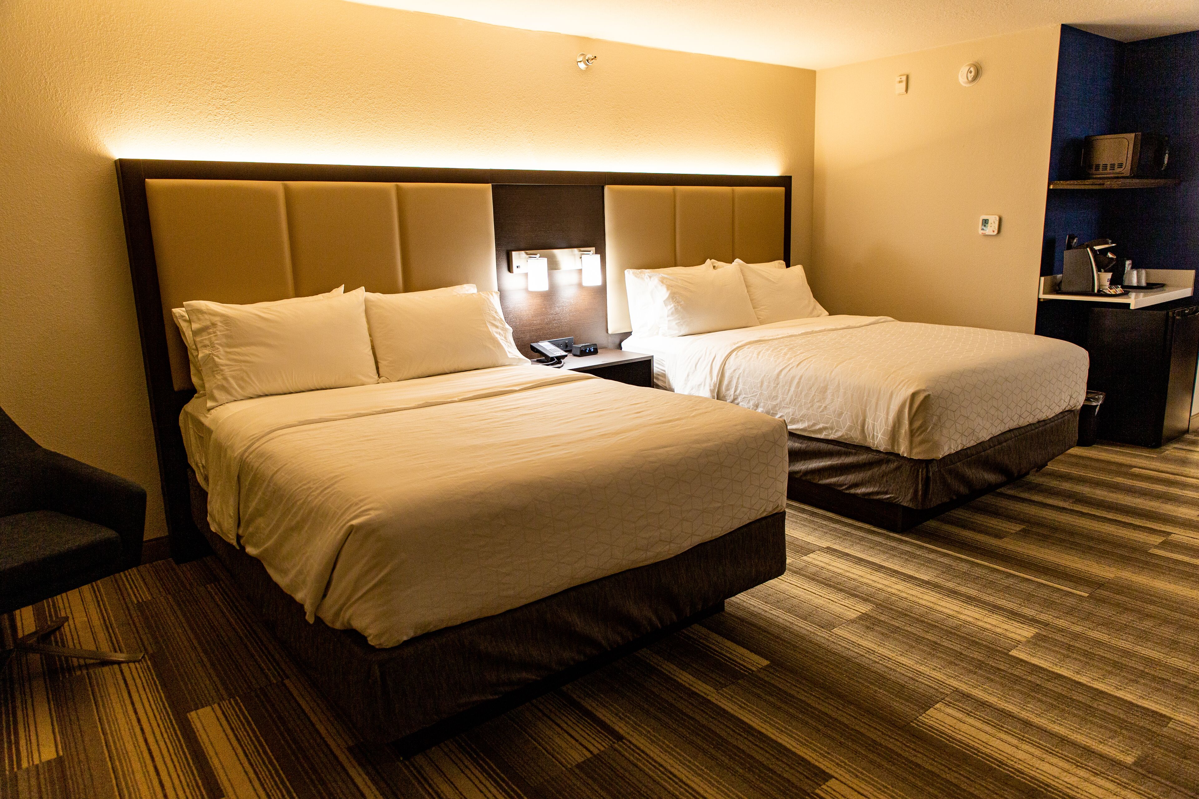 A hotel room with two beds, a desk, a chair, and a microwave.