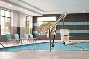 An indoor swimming pool with a pool lift, lounge chairs, and a view of trees through large windows. - Holiday Inn Express Hotel & Suites Norfolk Airport by IHG (Norfolk)