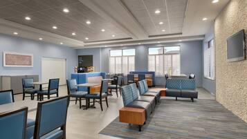 A modern hotel lobby with seating areas, a coffee station, and large windows.