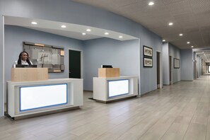 A hotel reception area with a receptionist, a reception desk, and a corridor with framed pictures on the wall. - Holiday Inn Express Hotel & Suites Norfolk Airport by IHG (Norfolk)